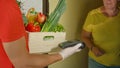 CLOSE UP: Courier holds produce and a payment terminal while waiting for lady