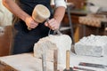 Bearded craftsman works in white stone carving with a chisel. Creative workshop with works of art. Royalty Free Stock Photo