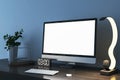 Close up of creative designer desktop with empty white mock up computer monitor, supplies and various items on blue concrete wall Royalty Free Stock Photo