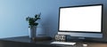 Close up of creative desktop with empty white mock up computer monitor, supplies and various items on blue concrete wall