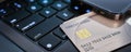 Close-up of a credit card placed on a laptop keyboard next to a smartphone displaying financial information.