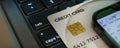 Close-up of a credit card placed on a laptop keyboard next to a smartphone displaying financial information.
