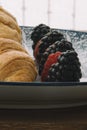 close-up of a croissant with blackberries and raspberries on a Mediterranean print plate