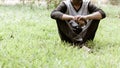 Close up Cropped image of young man in casual clothing sitting over green grass in the park at morning time of day. Front view. Royalty Free Stock Photo