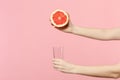 Close up cropped photo of female holding in hands half of fresh ripe grapefruit, glass cup isolated on pink pastel wall Royalty Free Stock Photo