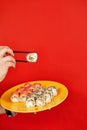 Close up cropped photo of male hold in hands makizushi sushi roll served on plate traditional japanese food isolated on Royalty Free Stock Photo