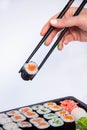 Close-up cropped photo shot of women`s hand person hold chopsticks delicious sushi rolls served on plate with white background