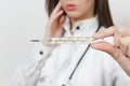 Close up cropped sad upset doctor woman in medical gown with stethoscope. Focus on clinical thermometer with high fever