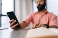 Close-up cropped shot of unrecognizable bearded businessman in pink clothes using mobile phone sitting at office desk