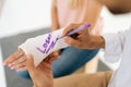 Close-up cropped shot of unrecognizable male funny doctor writing joking inscription on cast of woman with broken hand Royalty Free Stock Photo