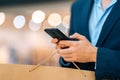 Close-up cropped shot of unrecognizable young man in stylish suit using mobile phone standing in hall of mall center Royalty Free Stock Photo