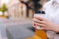 Close-up cropped shot of unrecognizable young woman holding in hands paper cup with takeaway coffee sitting on bench on Royalty Free Stock Photo