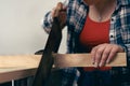 Close-up cropped shot of a young red-haired female carpenter, sawing a plank of wood in her small workshop.