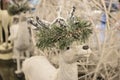 Close-up cropped white sparkly reindeer Christmas decoration with garland of snow covered greenery around horns - selective focus