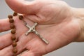 Close-up of the crucifix of a wooden rosary in the hand of an elderly woman