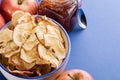 Close-up cup with apple chips, fresh apples and jar of apple jam and metallic spoon on blue background