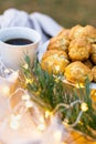 Close-up of a cup of coffee with cakes on a table with a fir branch and garland lights