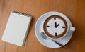 Close up of A Cup hot latte art coffee drawn an o`clock business concept on wooden table with note book