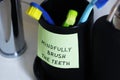 Close-up of a cup for toothbrushes with a sticker containing a handwritten inscription: Mindfully brush the teeth