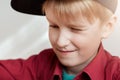 A close-up of curious little boy with white hair wearing stylish black hat and red shirt looking at something with narrowed eyes. Royalty Free Stock Photo