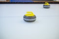 Close-up of a curling stone with a yellow handle stands on ice