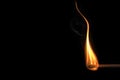 Close up of a curving flame of a match against a black background