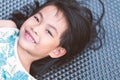 Close up of cute Asian child girl, smiling face, black long hair, lay down on wicker beach chair and looking at camera Royalty Free Stock Photo