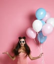 Close-up of cute blond girl standing in a studio, smiling widely and playing with blue and pink baloons.