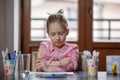 Blond hair school girl boring and tired looking up, sitting at the desk with school supplies, holding colored pencils in her hands Royalty Free Stock Photo