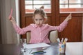 Blond hair school girl, sitting at the desk with school supplies and with her hands raised up Royalty Free Stock Photo