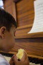 Close up of cute boy eating apple while sitting by piano Royalty Free Stock Photo