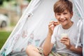 Close up of cute  boy eating cookie, smiling, holding glass of milk. looking at camera, eye contact Royalty Free Stock Photo