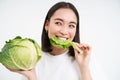 Close up of cute korean woman, eating cabbage, on diet, holding lettuce, isolated on white background Royalty Free Stock Photo