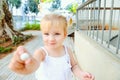 Close up cute little blondy toddler girl in white dress giving small sweet round candy for you. Selective focus. Copy space.