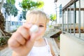 Close up cute little blondy toddler girl in white dress giving small sweet round candy for you. Selective focus. Copy space.