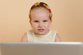 Close up of a cute little girl looking at camera, holding a laptope, over beige background. Horizontal view Royalty Free Stock Photo