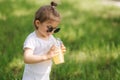 Close-up of cute little girl in white bodysuit and sunglasses drink lemonade outdoors