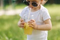Close-up of cute little girl in white bodysuit and sunglasses drink lemonade outdoors