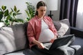 Close up of cute pregnant woman sitting on cozy sofa working from home, typing on pc laptop at big belly indoors, using online app Royalty Free Stock Photo