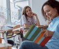 Close up cute schoolgirl smiling while young tutor is reading her. Elementary school kids sitting on desks in classroom Royalty Free Stock Photo