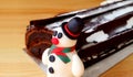 Close-up of a Cute Snowman Marzipan with Blurred Chocolate Yule Log Cake in Background Isolated on Wooden Table Royalty Free Stock Photo