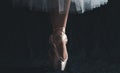 Close-up of dancing legs of ballerina wearing white pointe on a black background