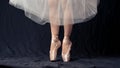 Close-up of dancing legs of ballerina wearing white pointe on a black background