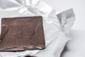 Close up of Dark brown chocolate square cracked on silver foil on a white background Royalty Free Stock Photo