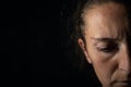 Close-up of a dark portrait of a very dimly lit woman. The woman has a frown and is looking down, conveying a feeling of sadness