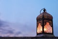 Close-up of dark silhouette of glowing ornamental Moroccan lantern. Blurred evening sky, dusk. Festive still life for