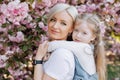 Close up of daughter hugging mom sitting on her back on cherry sakura background. Walk in the sakura trees in the city