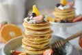 Close-up, Decorating a stack of pancakes by baker hands with blueberries, strawberries, orange and whipping cream.