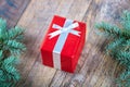 Close-up red present box on a wooden and pine branch background. Christmas celebration concept.