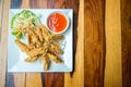 Close up deep fried chicken wings with vegetable side dish and chili sauce, served on the white dish on wood table. Royalty Free Stock Photo